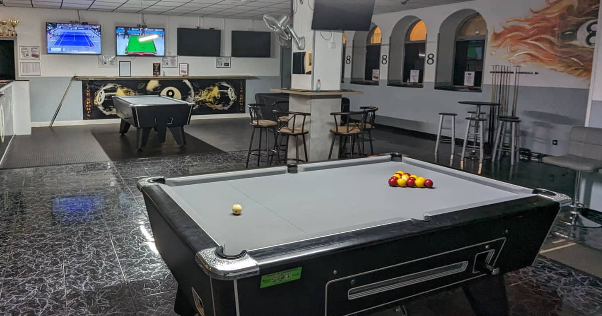 Bar pool table with red and yellow balls racked, stools and screens behind