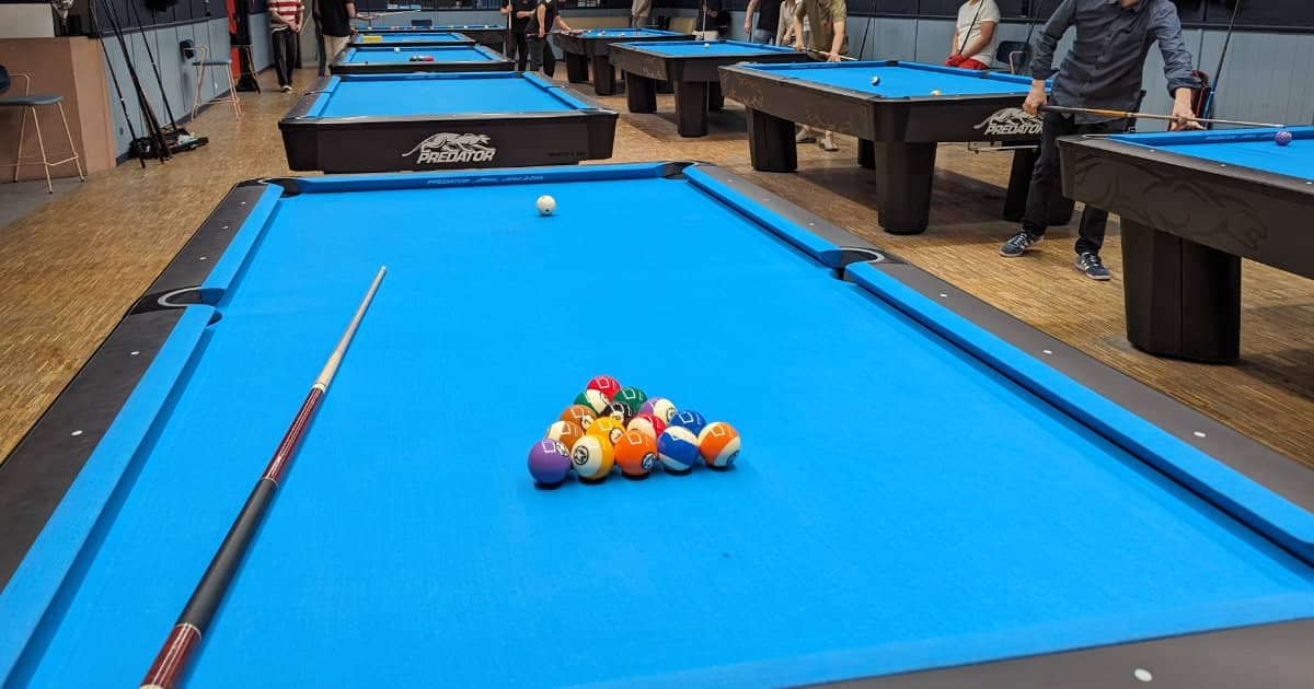 American pool table with racked numbered balls and a cue in a pool hall