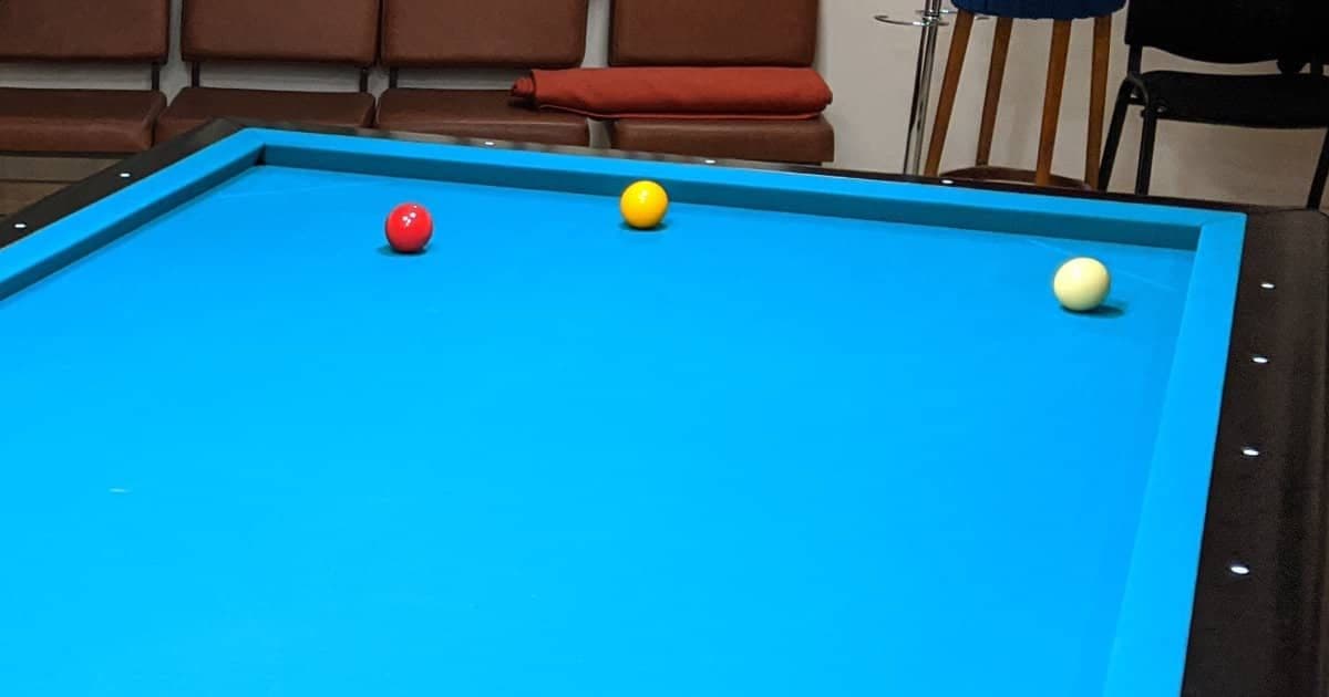 Pocketless carom table with blue cloth and the red, yellow and white balls