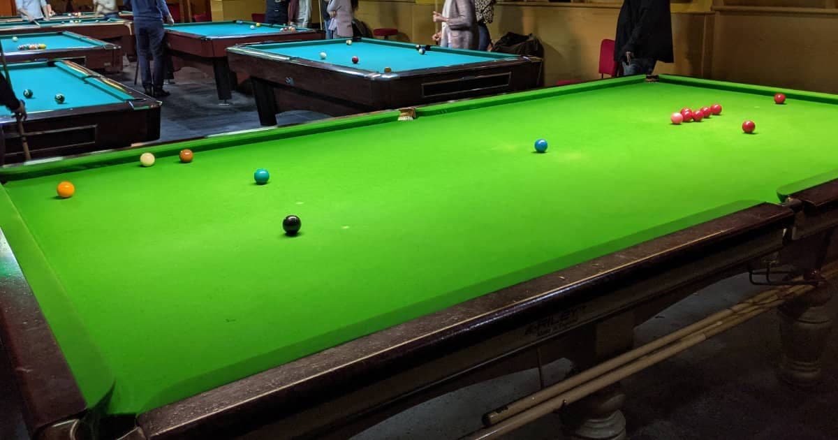Full-size snooker table with reds and colours in play, pool tables in the background