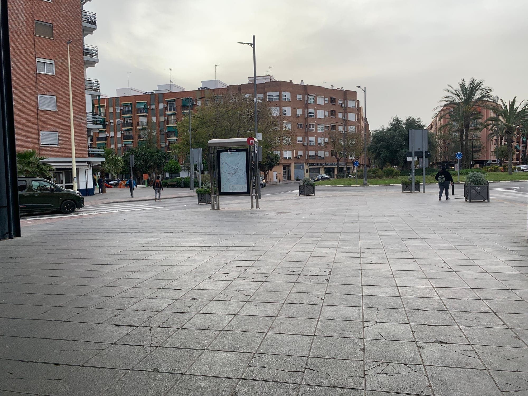Paved square with a metro map stand, brick apartment blocks and a roundabout in Quart de Poblet, Spain
